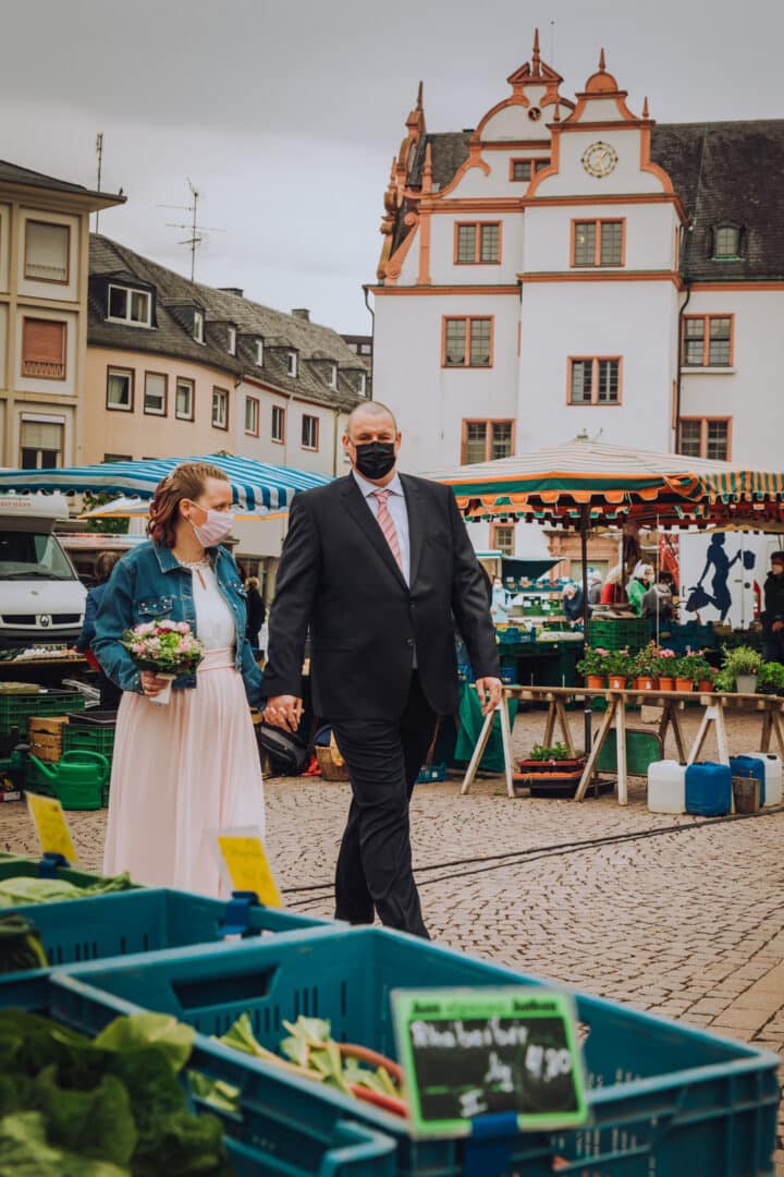 Brautpaar läuft über den Marktplatz zwischen den Marktständen entlang