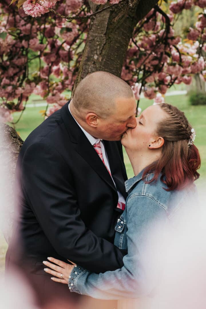 Braut und Bräutigam küssen sich unter dem blühenden Kirschbaum im Herrngarten Darmstadt