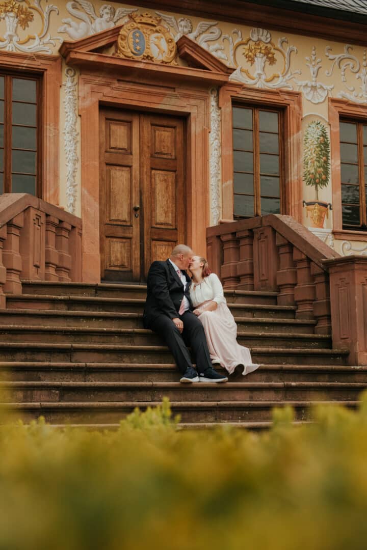 Braut und Bräutigam sitzen auf einer Treppe im Prinz-Georg Garten Darmstadt und küssen sich.