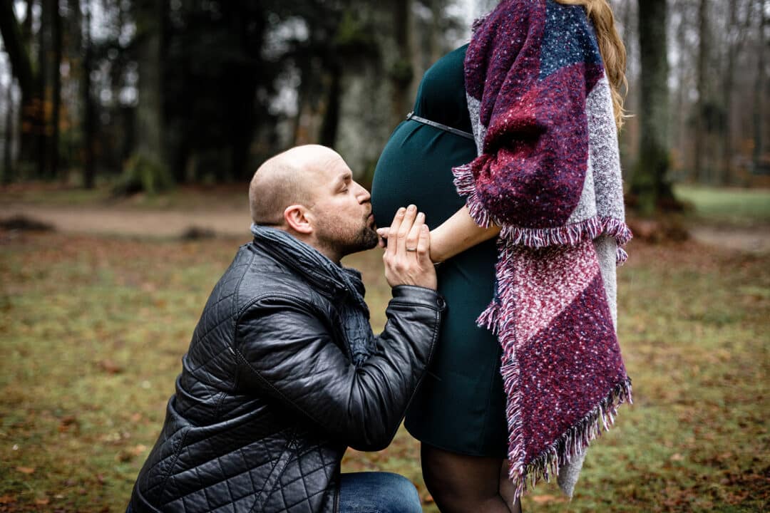 Mann küsst den Babybauch seiner Frau im Park bei Regen