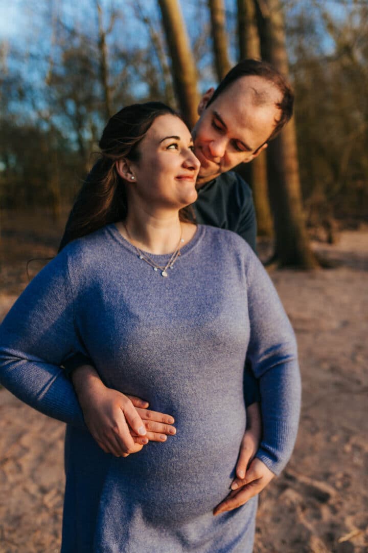 Mann und Frau halten ihren Babybauch und er schaut sie an