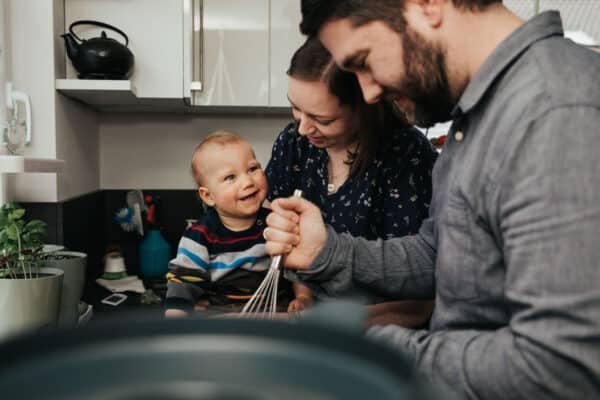 Eine Familie zu dritt ist in der Küche und backt zusammen während der kleine Junge freudig lacht.