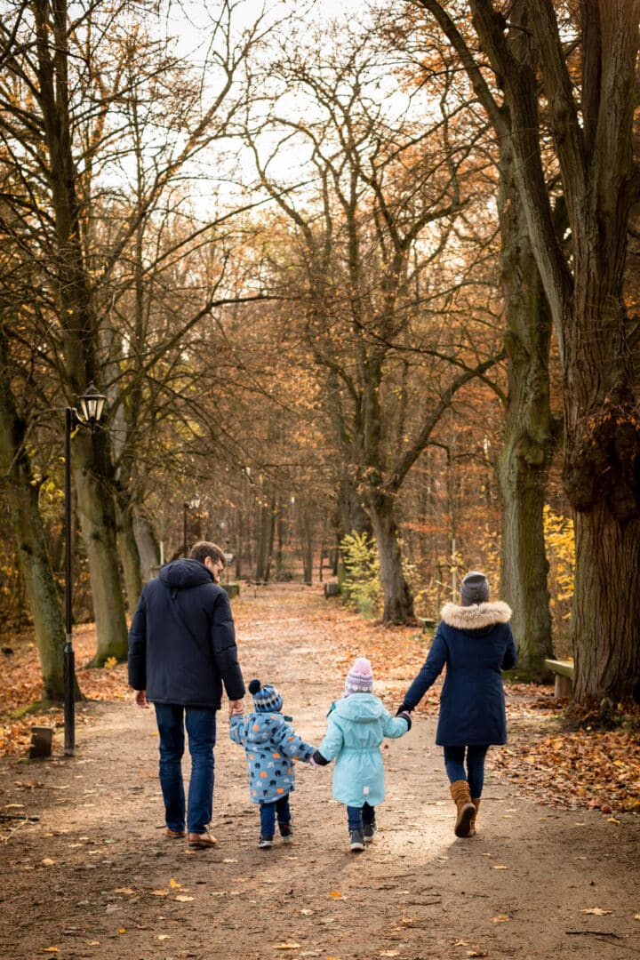 Familie läuft zu viert Händehaltend mit Rücken zur Kamera im Herbstwald