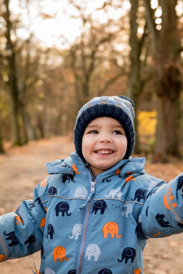 Kleiner Junge in blau wird an Hand gehalten während er durch den Herbstwald läuft