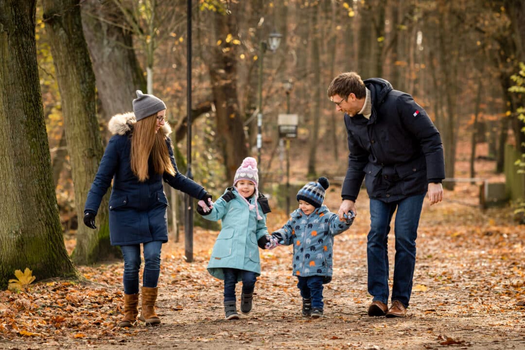 Familie zu viert hält ihre Kinder an den Händen und läuft durch das Herbstlaub