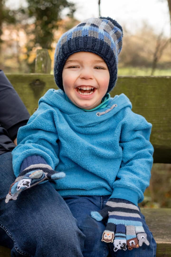 Junge mit blauem Pullover sitzt lachend auf Bank im Herbst