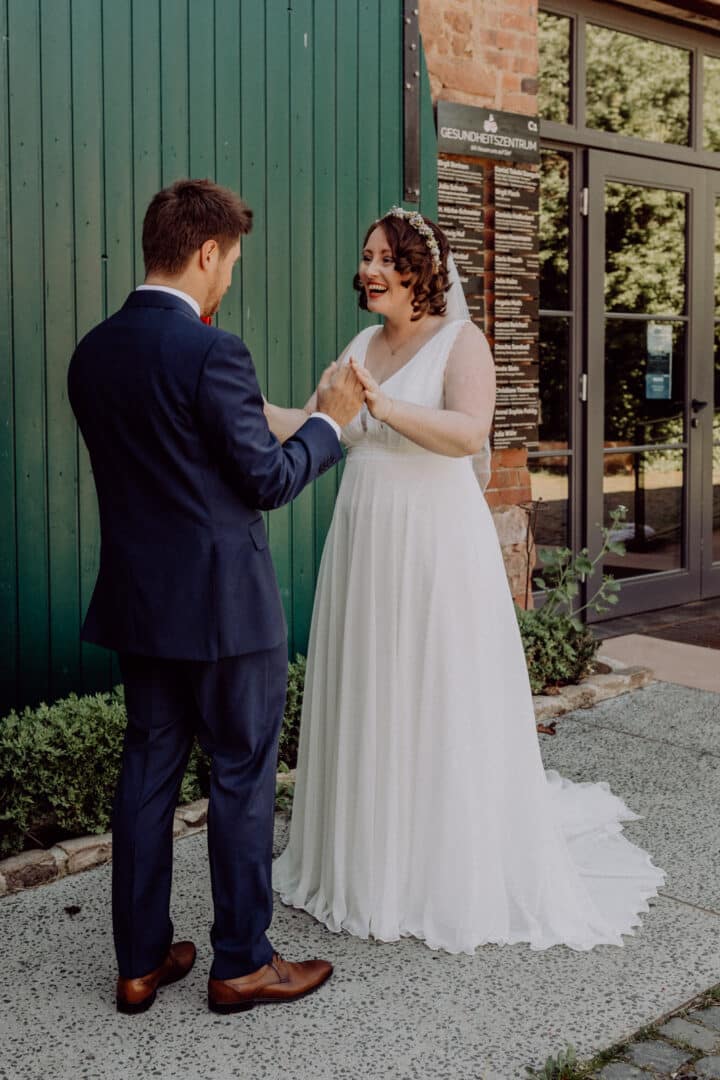 Braut hält die Hand ihres Mannes als sie ihn beim First Look das erste Mal sieht und lacht.