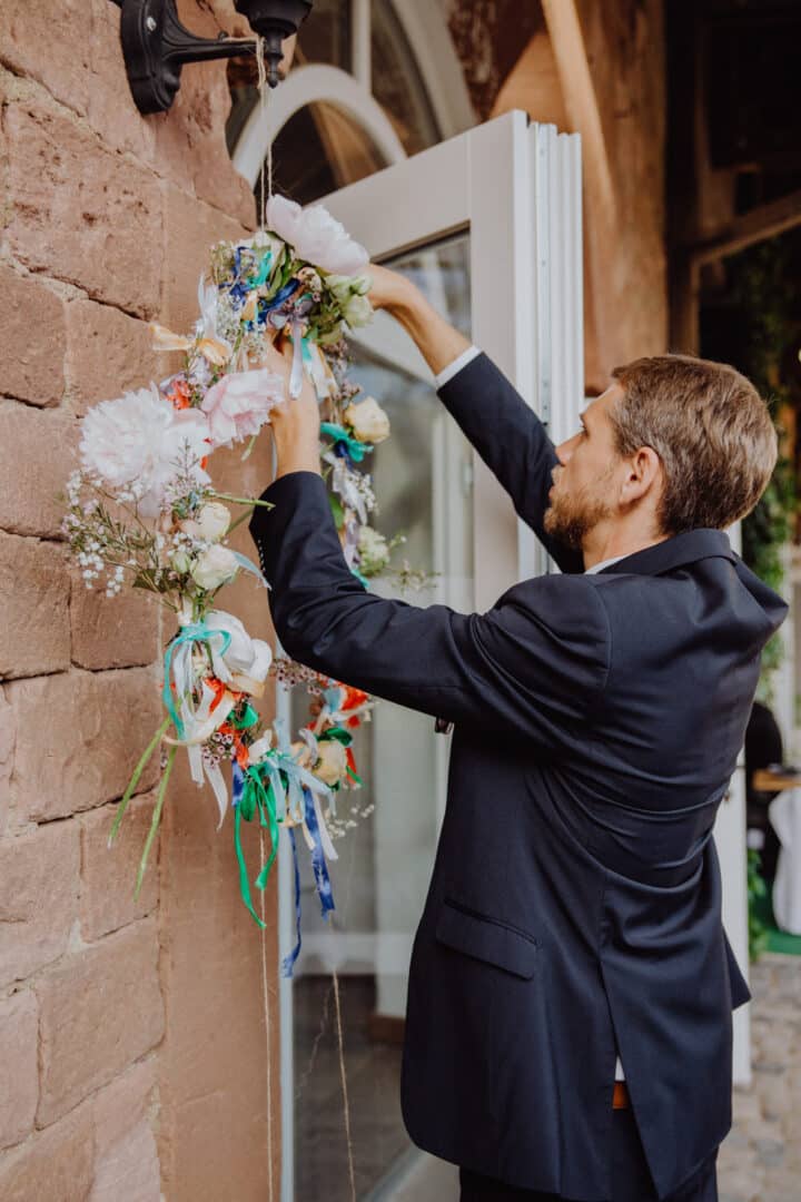 Mann bringt Blume am hängenden Blumenkranz auf einer Hochzeit auf dem Hofgut Habitzheim an.