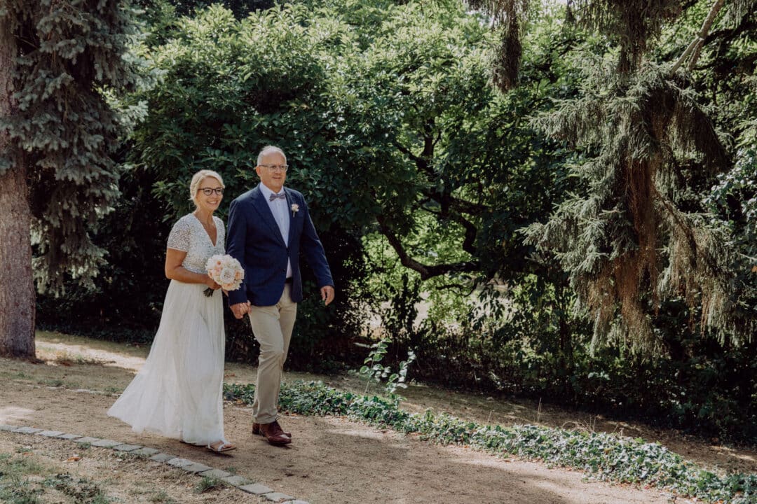 Brautpaar läuft auf dem Gartenweg des Hofgut Dippelshof zu ihrer Trauung