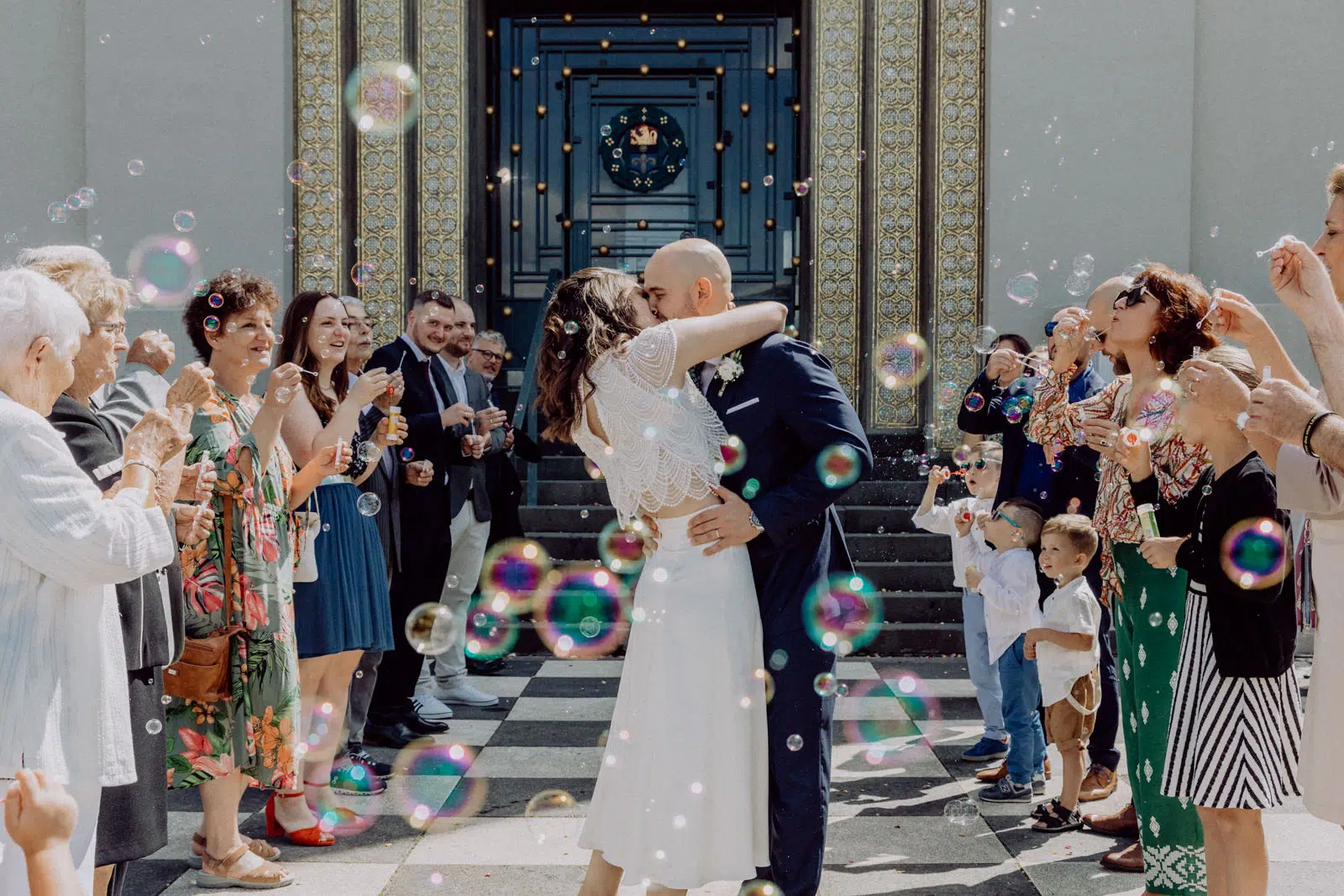Das Brautpaar küsst sich vor dem Hochzeitsturm Darmstadt und wird im Spalier der Gäste mit Seifenblasen empfangen.