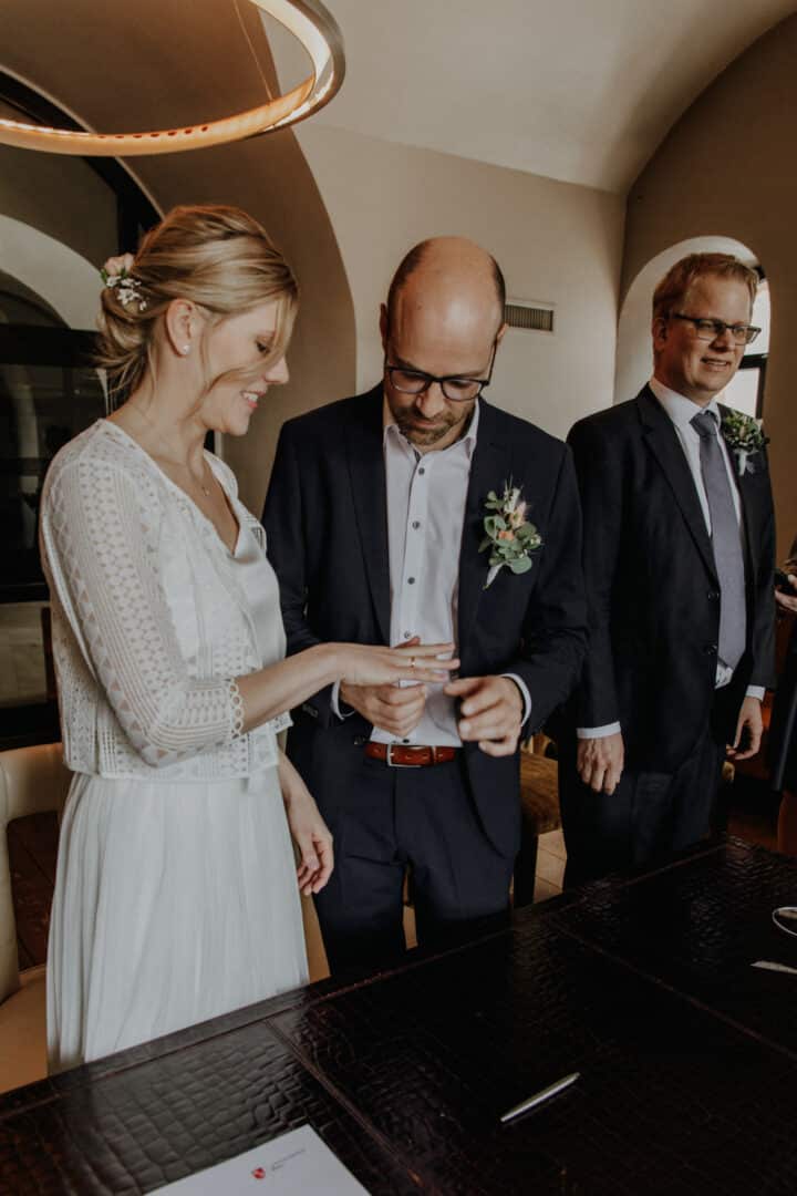 Der Bräutigam steckt seiner Frau den Ring an.
