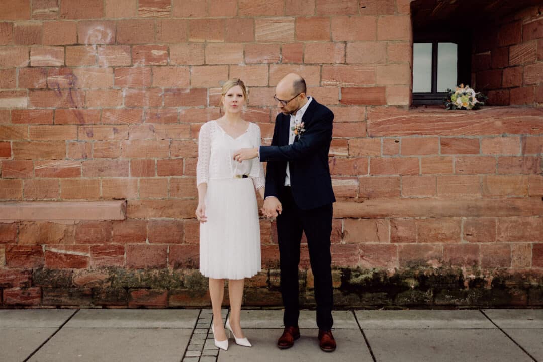Brautpaar lacht sich an und steht vor einer braunen Mauer des Fort Malakoff in Mainz.