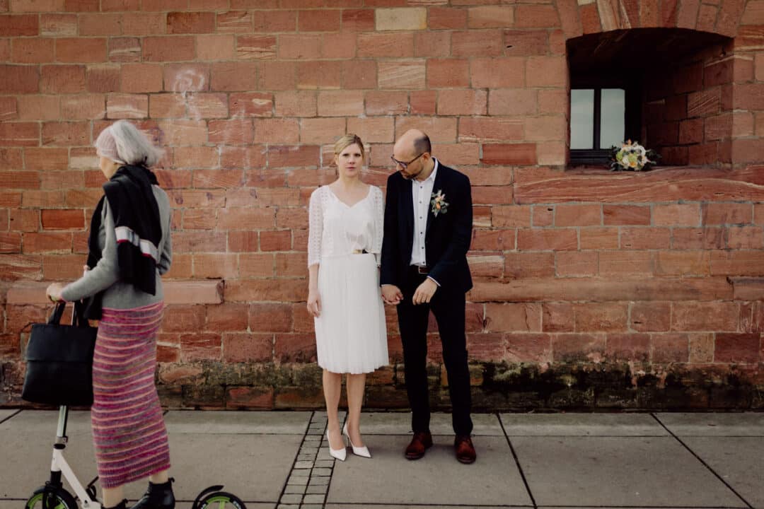 Brautpaar lacht sich an und steht vor einer braunen Mauer des Fort Malakoff in Mainz.