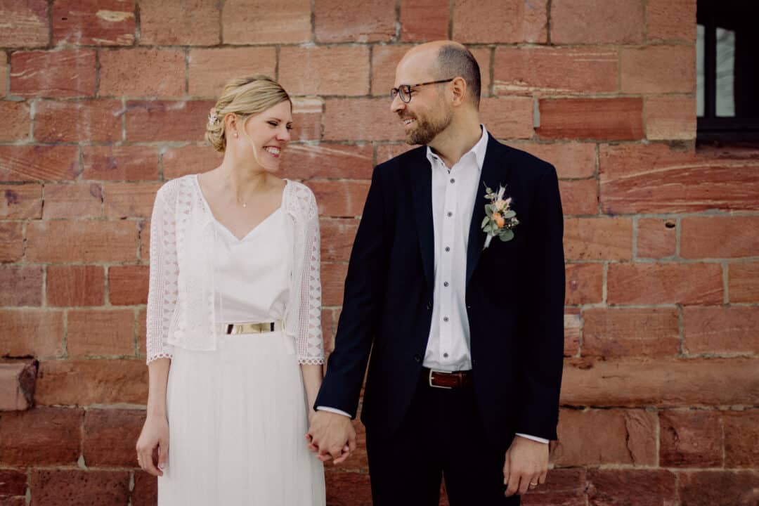 Brautpaar steht Hand in Hand lachend vor einer braunen Gesteinswand in Mainz