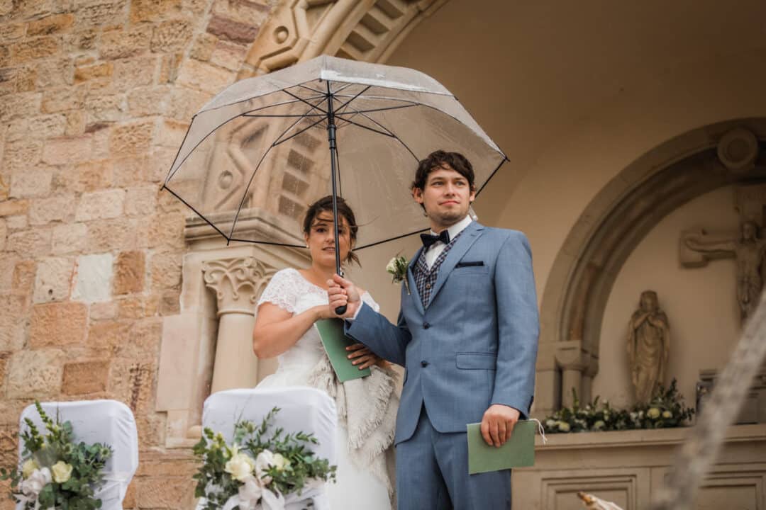 Trauung eines Brautpaares in der Kreuzkapelle Wißberg und Brautpaar steht mit Regenschirm da