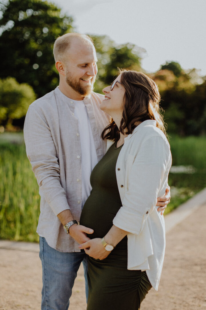 Ein Paar beim Babybauchfotoshooting in einem Park in Darmstadt beim Sonnenuntergang und lachen sich an.