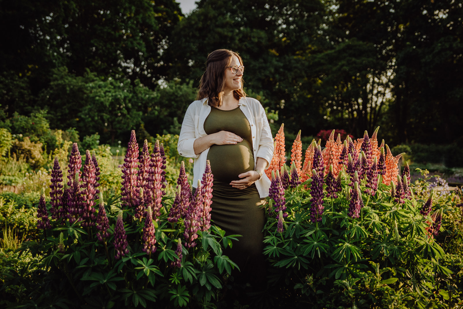 Eine Frau steht inmitten von Blumen und hält sich ihren Babybauch in einem Garten in Darmstadt.
