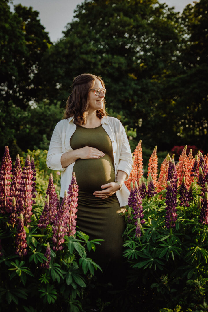 Eine Frau steht inmitten von Blumen und hält sich ihren Babybauch in einem Garten in Darmstadt.