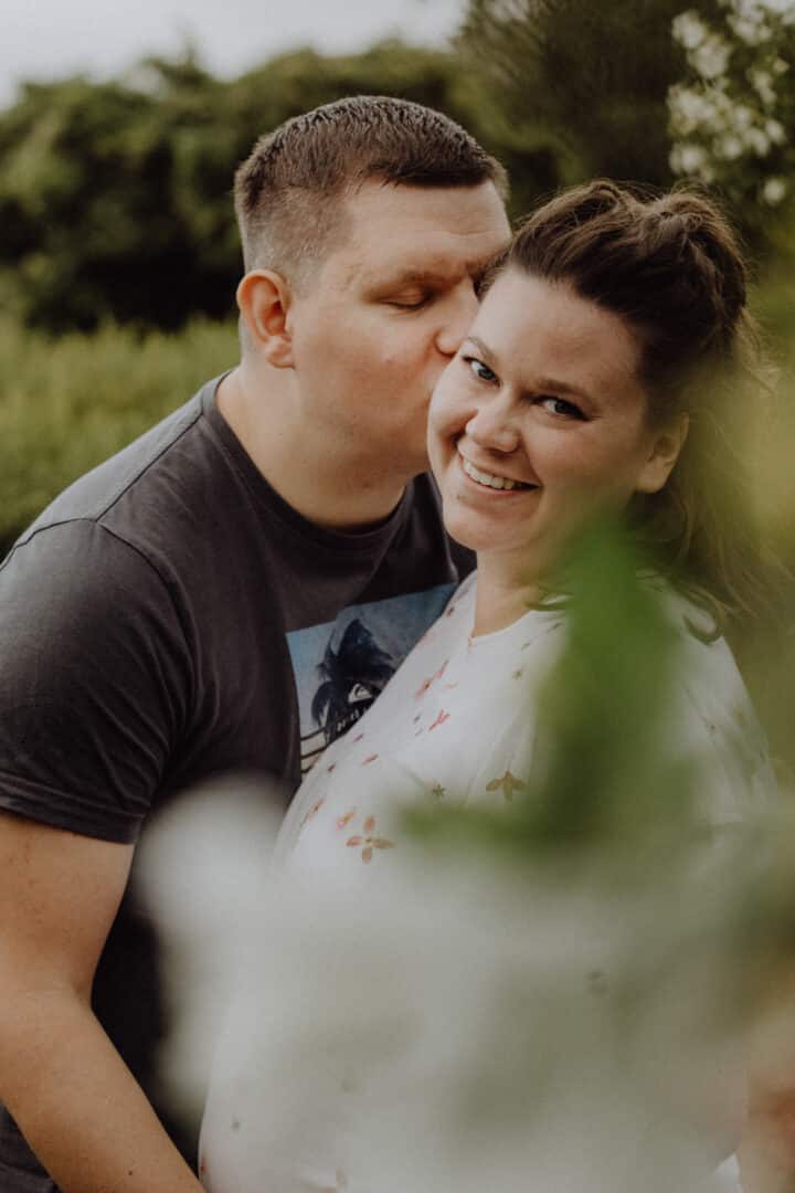 Partner küsst seine Frau beim Babybauch Fotoshooting in Darmstadt auf der Rosenhöhe.