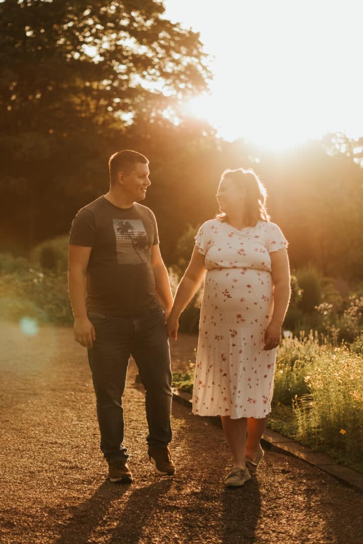Paar läuft beim Sonneuntergang Hand in Hand einen Weg entlang während ihres Babybauchfotoshootings in Darmstadt.