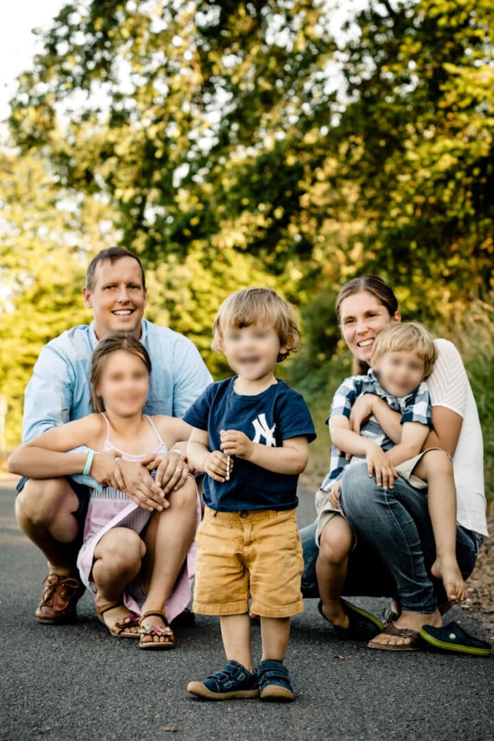 Familie sitzt auf einem Weg und ihr kleiner Sohn steht in der Mitte und lacht in die Kamera