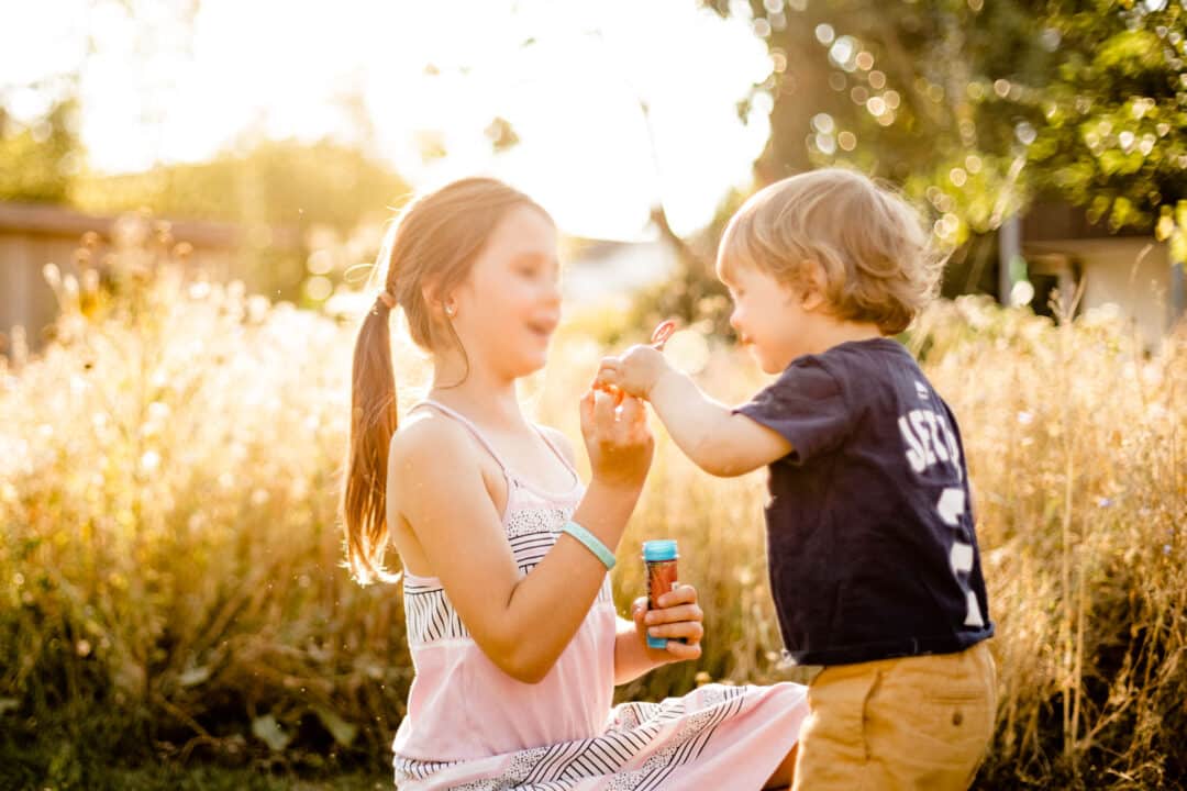 Zwei Kinder spielen draussen mit Gegenlicht und Seifenblasen