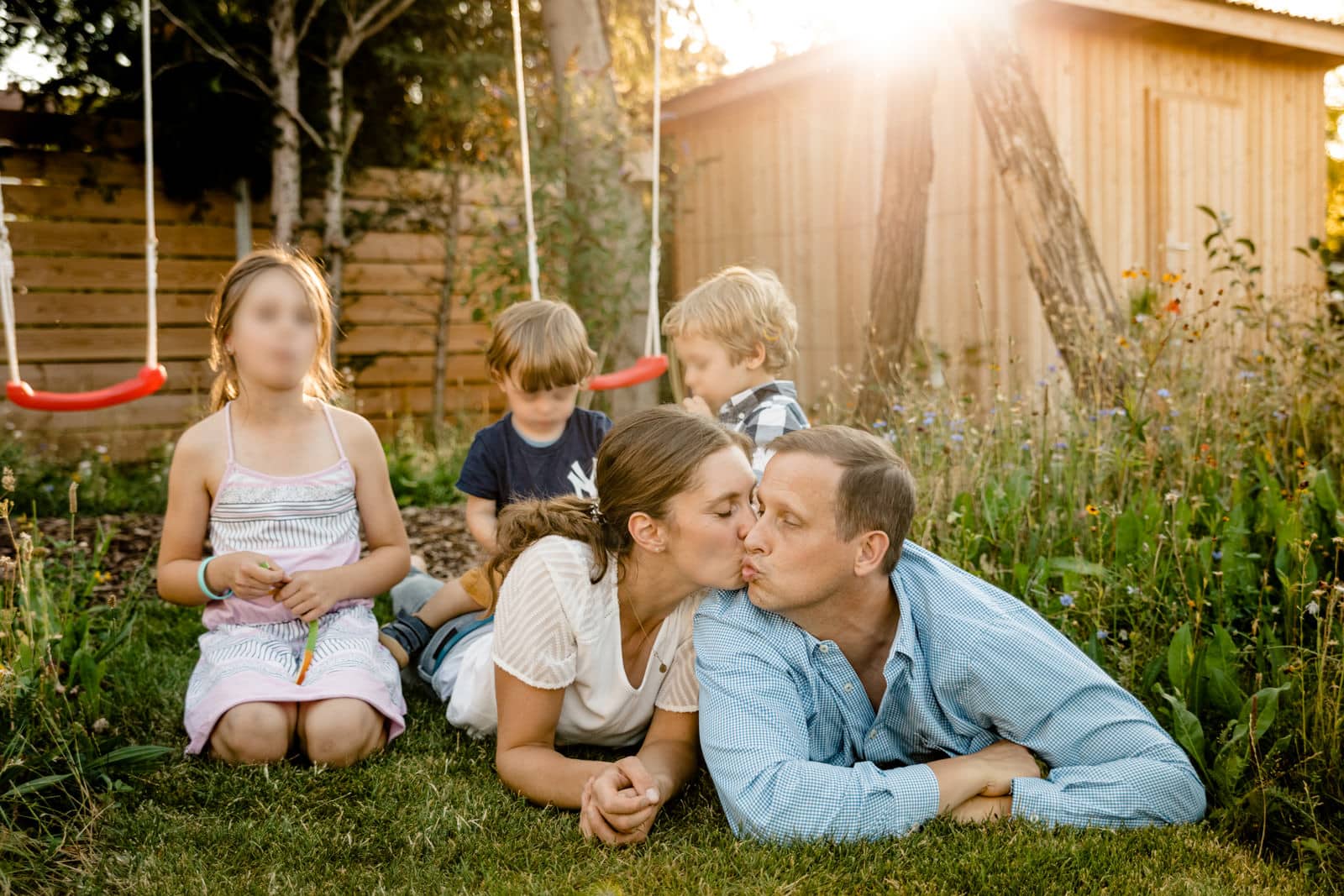 Eltern lieben auf dem Rasen und Küssen sich während die Kinder Süssigkeiten essen. Sonnenschein