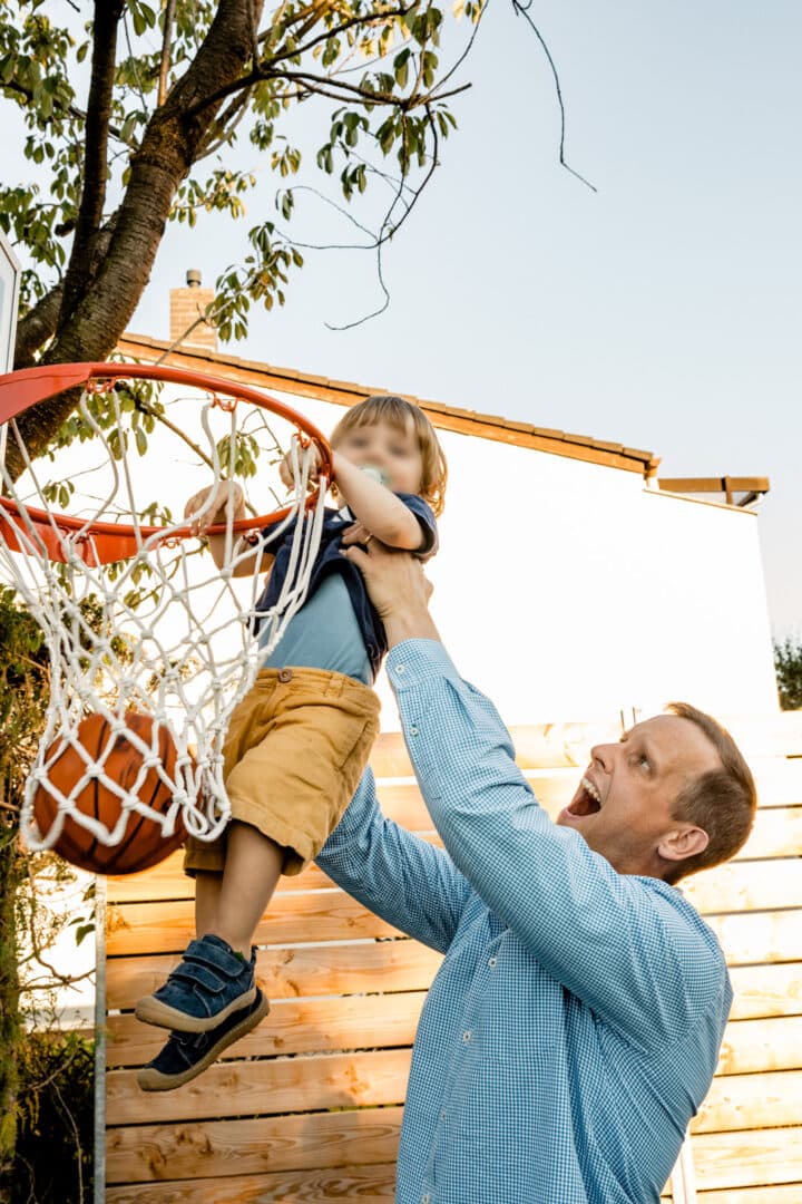 Vater hebt seinen Sohn zum Basketballkorb hoch zum Ball hinweinwerfen