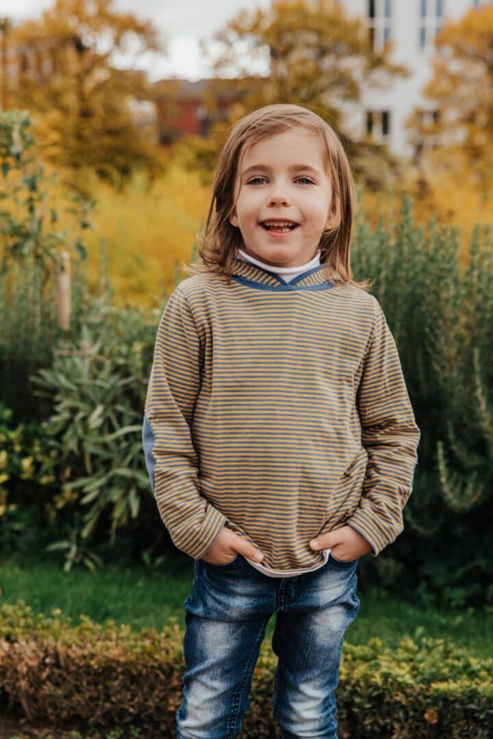 Ein kleines Mädchen im Park posed für die Kamera mit den Händen in der Hosentasche