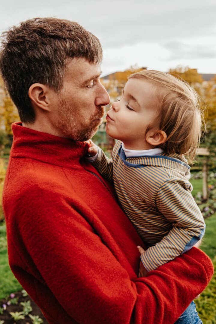 Ein Junge auf dem Arm seines Vaters küsst ihn