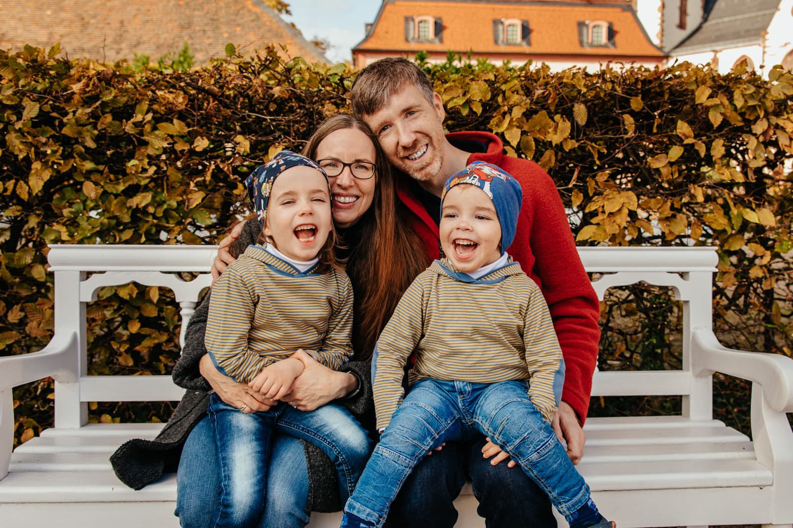 Eine vierer Familie sitzt auf einer Parkbank und lacht in die Kamera