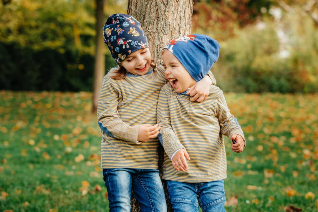 Zwei Geschwisterkinder halten sich im Arm und lachen im Park