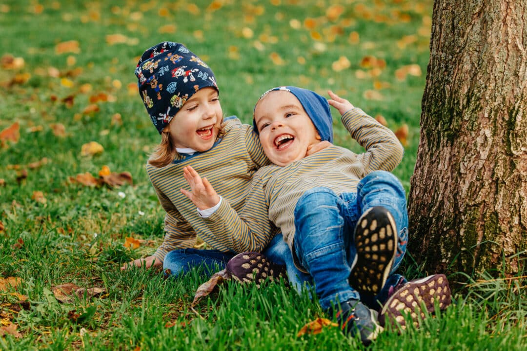 Zwei Geschwisterkinder liegen auf dem Rasen und lachen