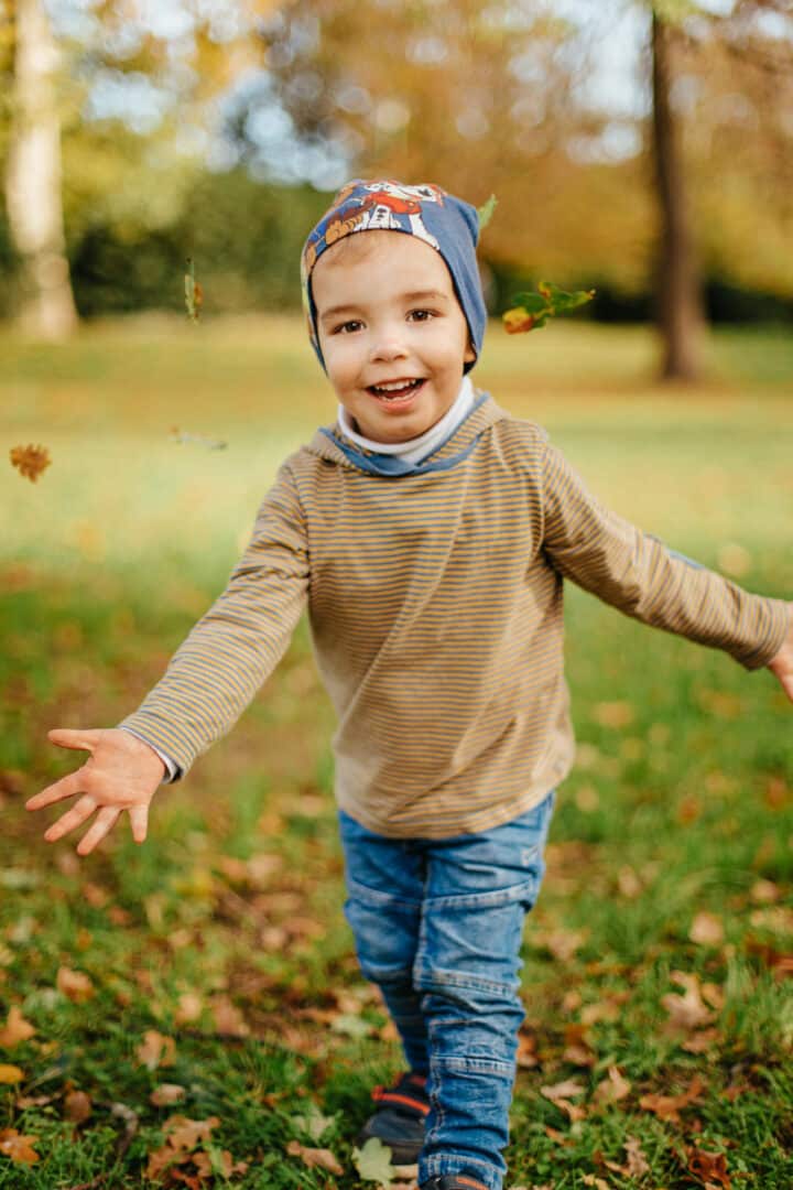 Ein kleiner Junge wirft lachend Herbstlaub nach oben