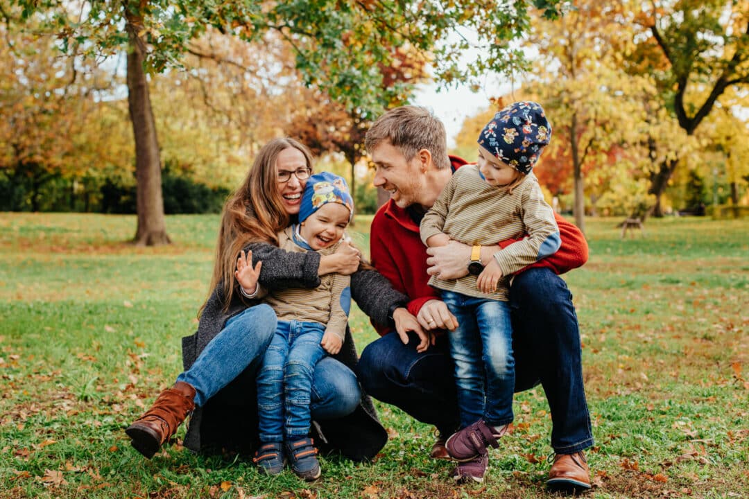 Eine Familie zu viert lacht mit ihren Kindern bei Familienfotos im Park