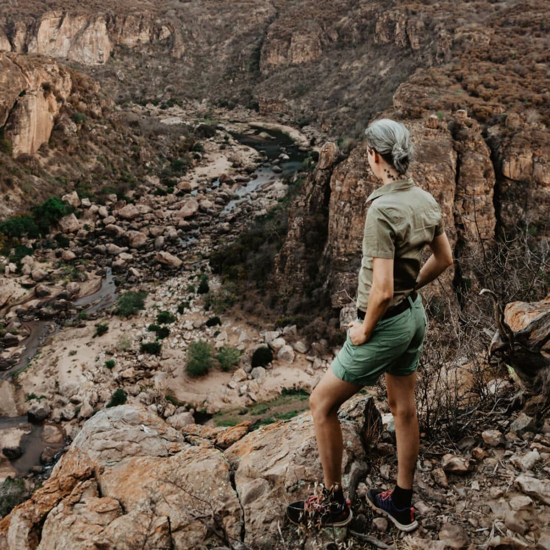 Frau steht in kurzer grüner Kleidung vor einer Schlucht in Afrika und schaut hinunter. Lanner Gorge.