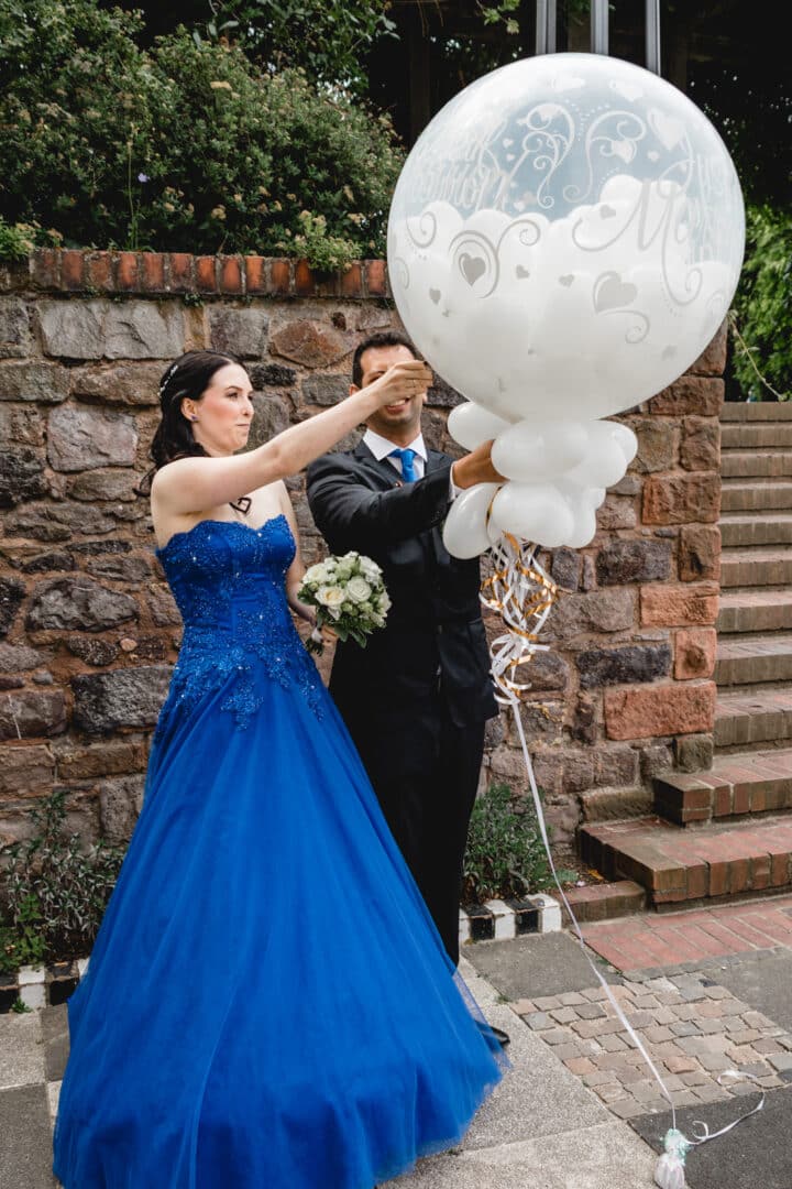 Brautpaar zersticht einen Luftballon und viele kleine weiße Herzluftballons fliegen weg