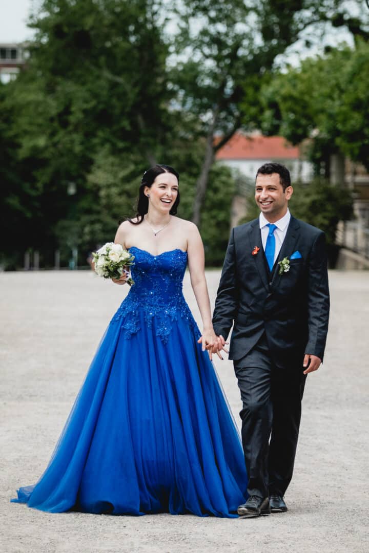 Eine Braut im blauen Brautkleid läuft zusammen mit ihrem Mann Hand in Hand auf der Mathildenhöhe in Darmstadt
