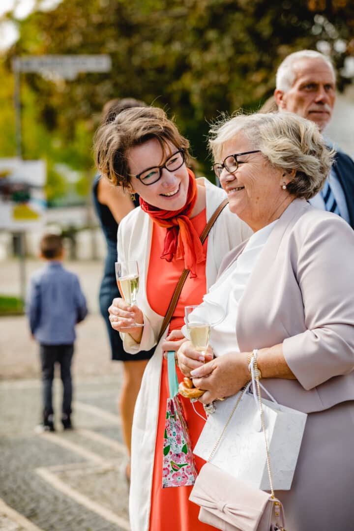 Zwei Frauen lachen mit Sekt in der Hand draussen vor der St. Ludwigs Kirche in Darmstadt während des Sektempfangs.