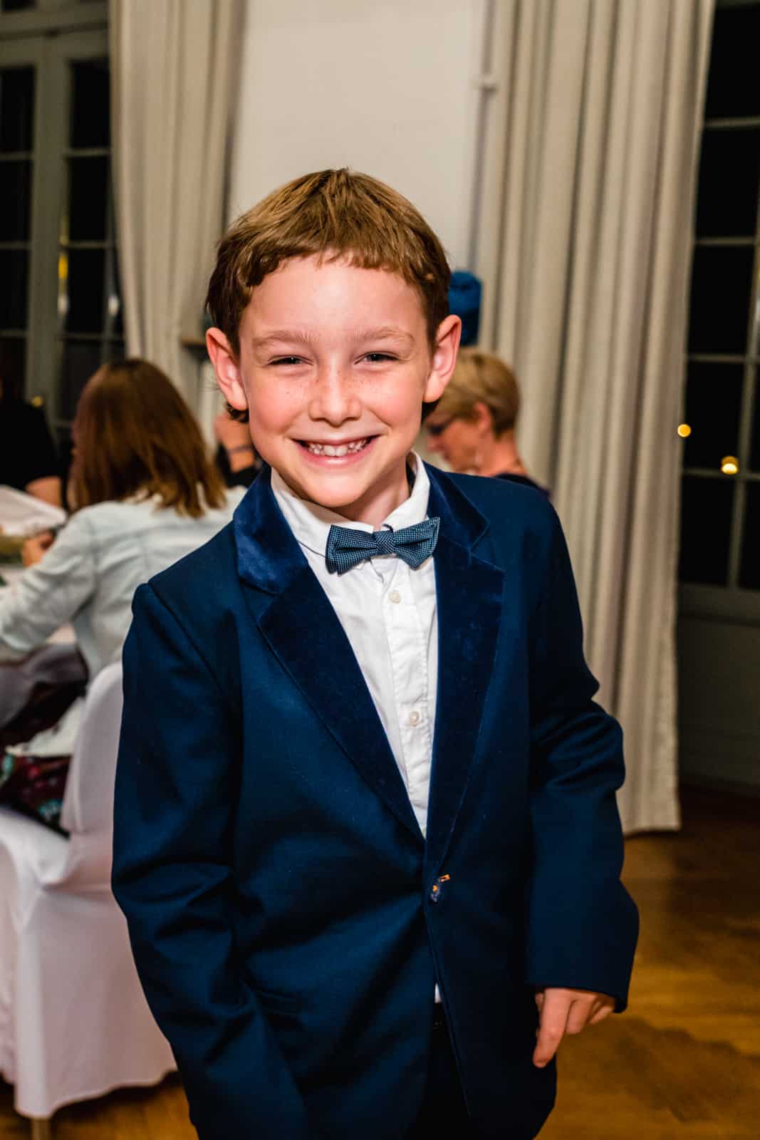 Ein Junge lacht bei einer Hochzeit in die Kamera und hat einen blauen Anzug an im Prinz-Emil-Schlösschen