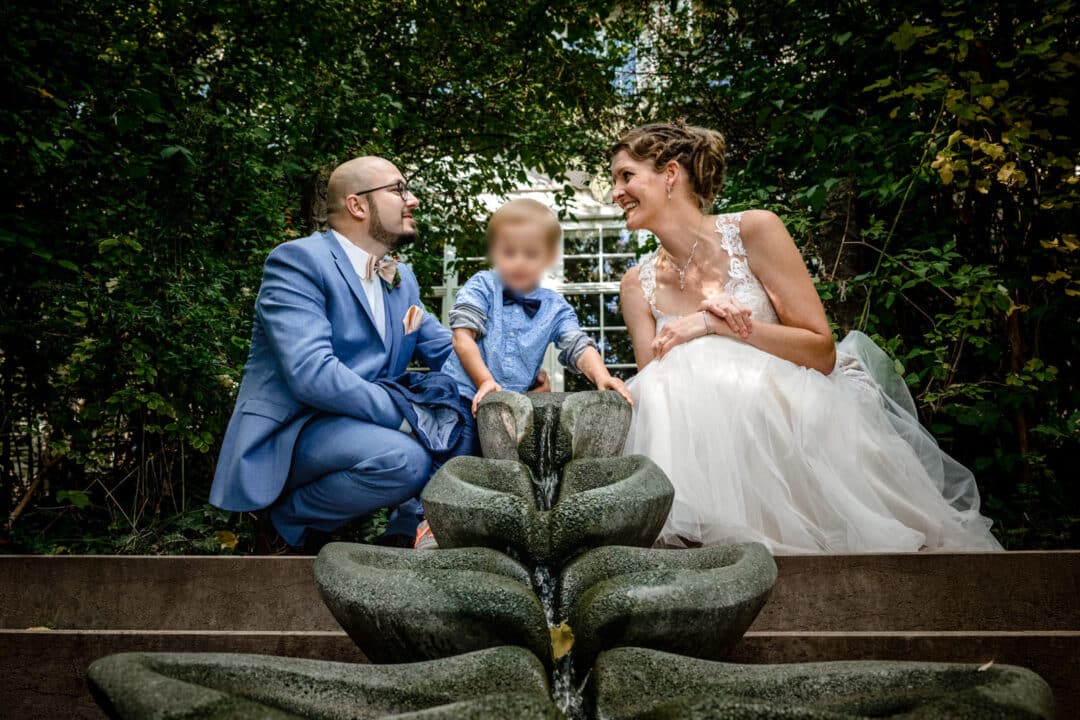Braut und Bräutigam sitzen vor Wasserfallinstallation und schauen ihrem Sohn zu