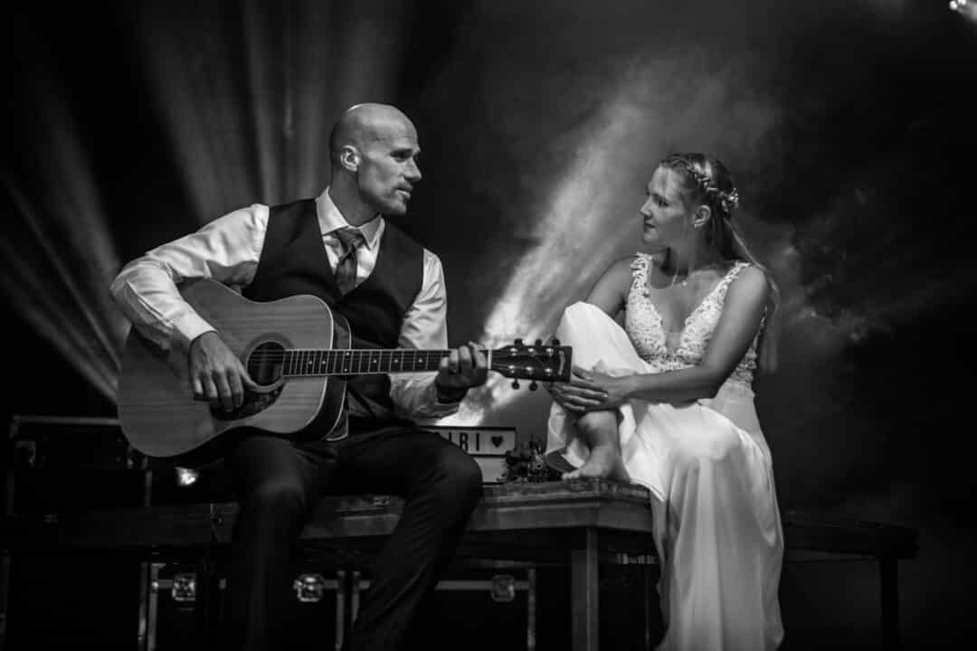 Braut hört ihrem Bräutigam zu während er ein Lied auf einer Gitarre zu ihr spielt.