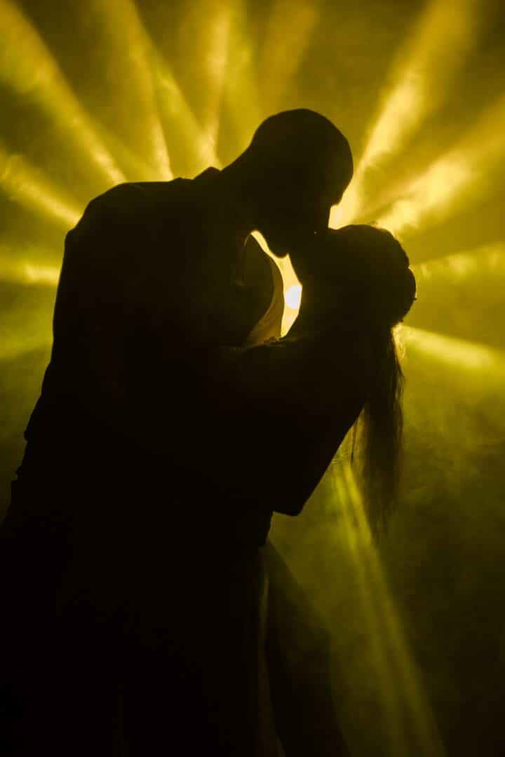 Brautpaar steht im schein eines gelben Scheinwerfers und die beiden Küssen sich als Silhouette