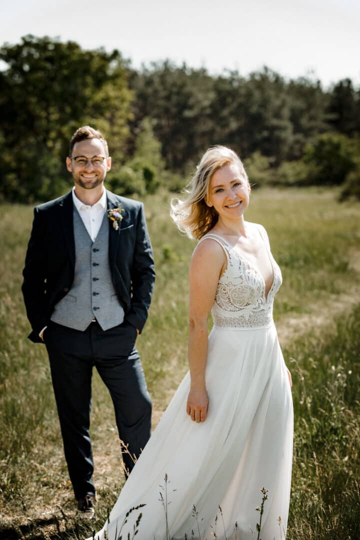 Braut lacht im Vordergrund mit Bräutigam im Hintergrund beim Outdoor Brautpaarshooting in den Griesheimer Dünen