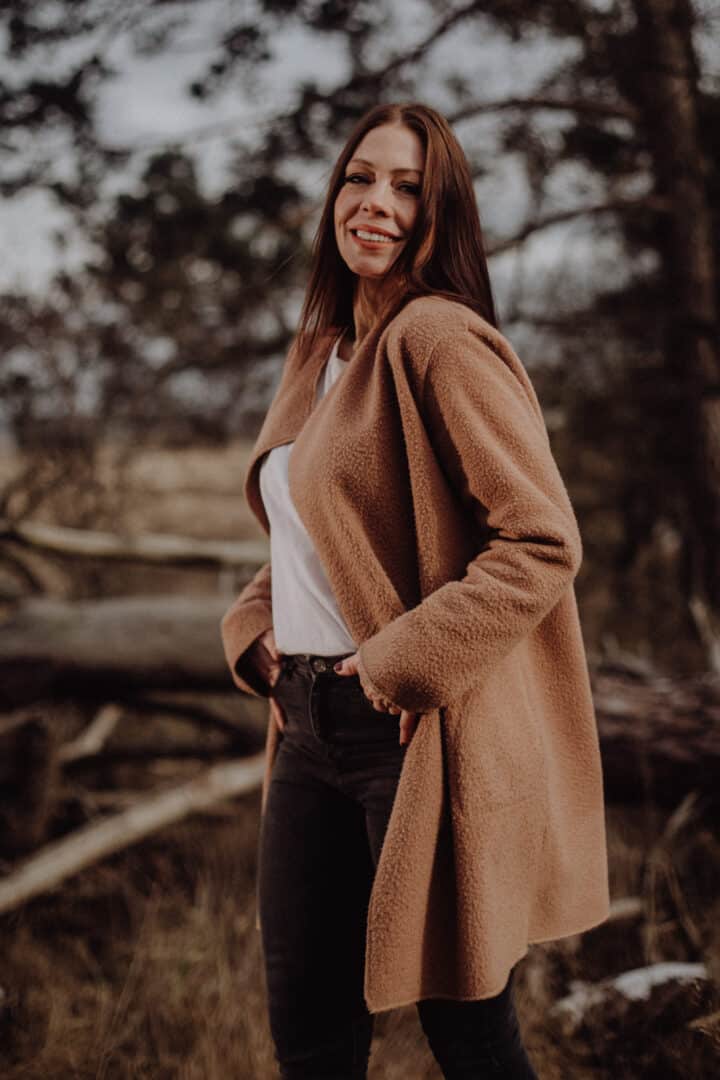 Eine Frau mit braunem Mantel lacht in die Kamera während ihres Fotoshootings.