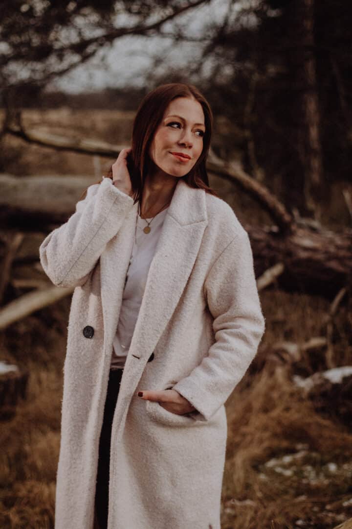 Frau beim Fotoshooting im Winter in der Natur mit weißem Mantel