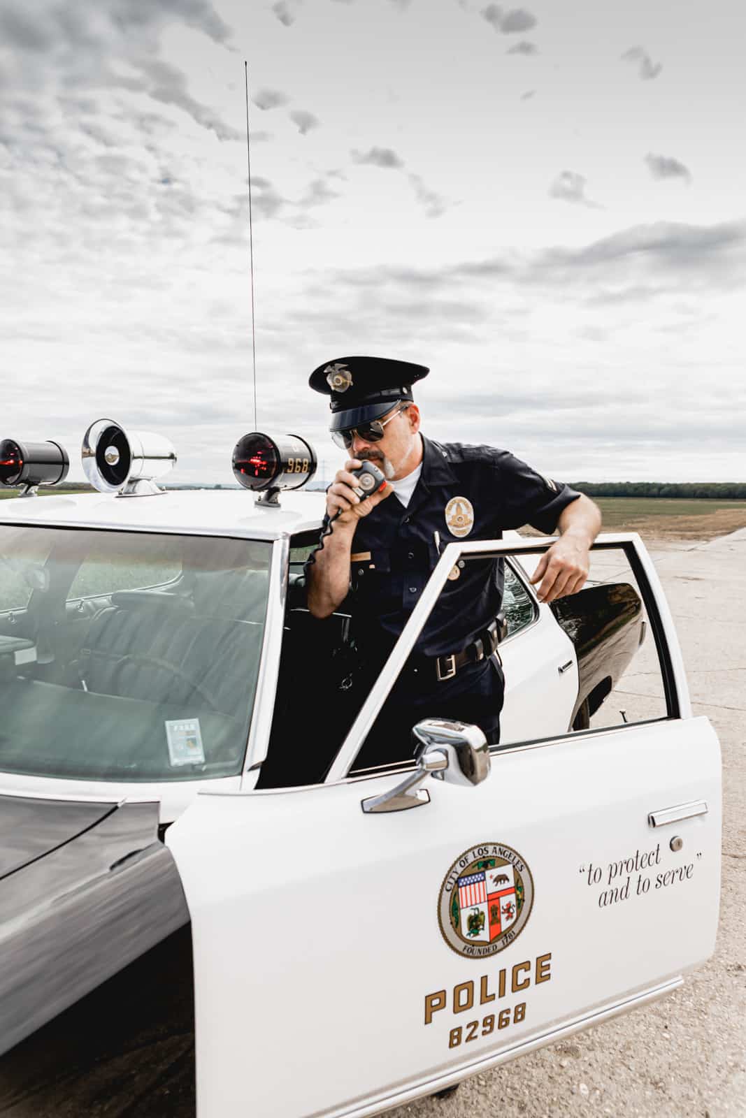 Ein amerikanischer Polizist steht an seinem Oldtimer Streifenwagen und spricht in sein Funkgerät in Gross-Gerau