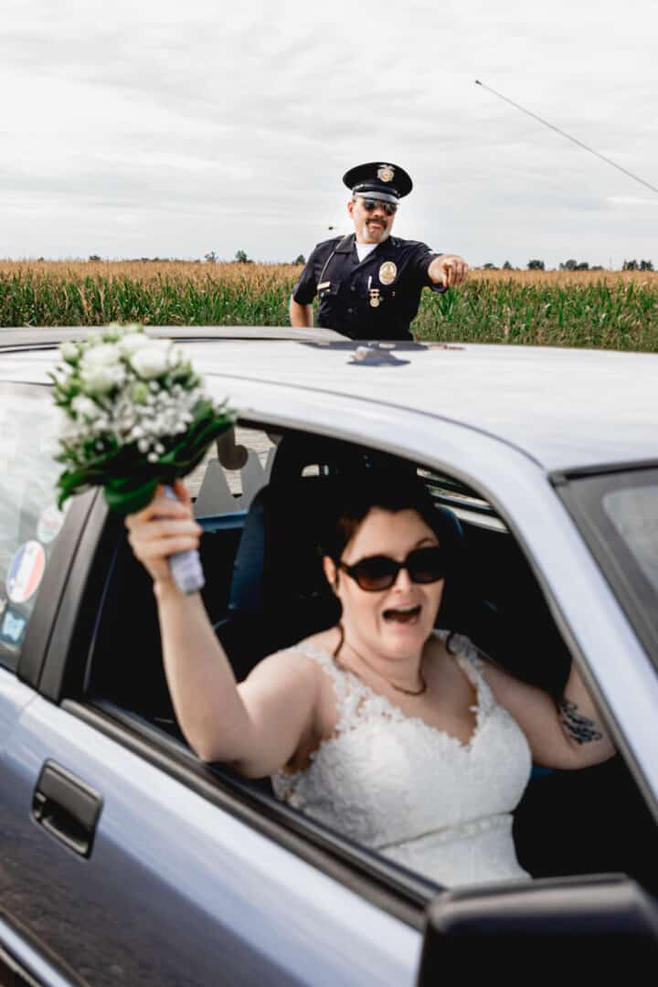 Braut hält die Hand mit Brautstrauß aus dem Fenster und Polizeiofficer zeigt was sie machen soll