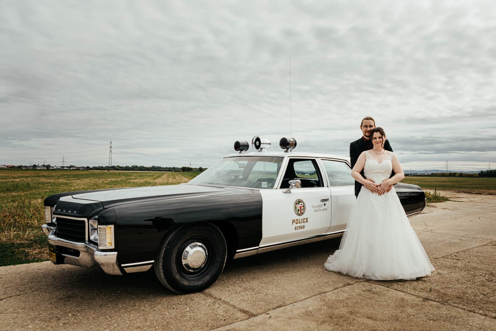 Brautpaar steht vor amerikanischem Polizeioldtimer