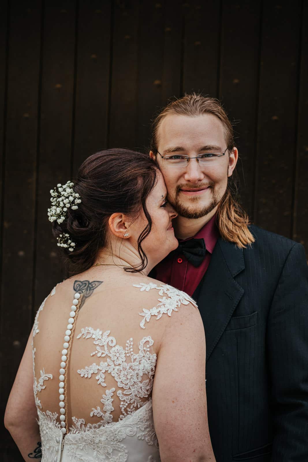 Bräutigam schaut in Kamera während sich seine Frau an ihn kuschelt